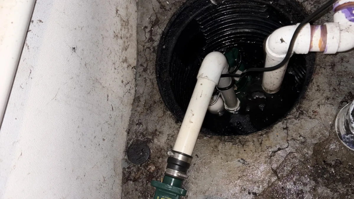 A sump pump installation area featuring a sump basin, pipes, and a pressure reducing valve during sump pump installation and pressure reducing valve in Bedford.